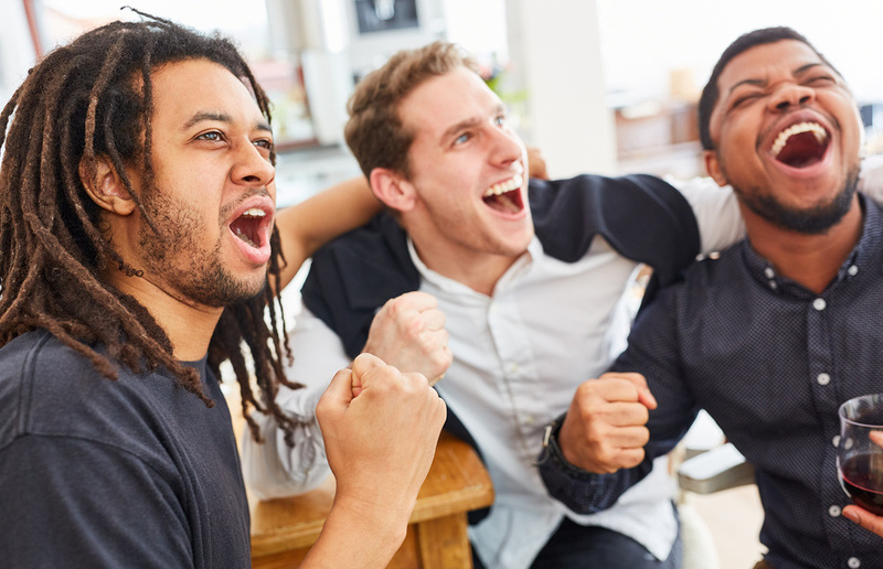 Befreundete Männer jubeln zusammen beim Fußball schauen / © Robert Kneschke, Robert Kneschke Befreundete Männer jubeln zusammen beim Fußball schauen zu Hause